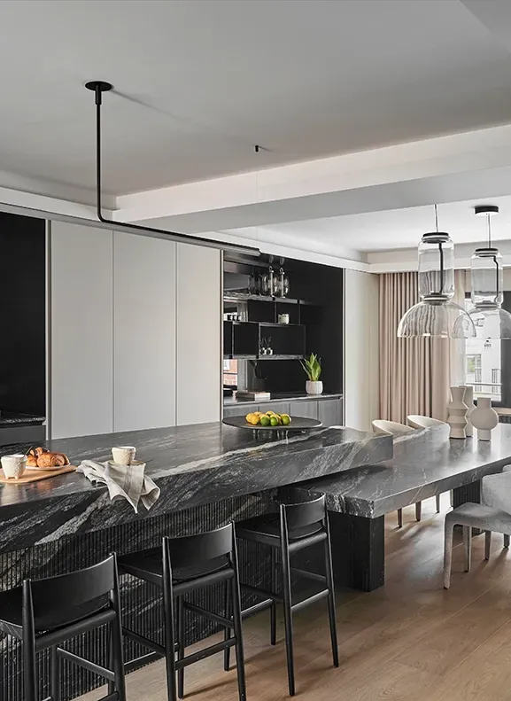 Spacious kitchen with striking stone countertop, long dining table, sculptural lighting, and ample natural light creating a bold, elegant contrast.