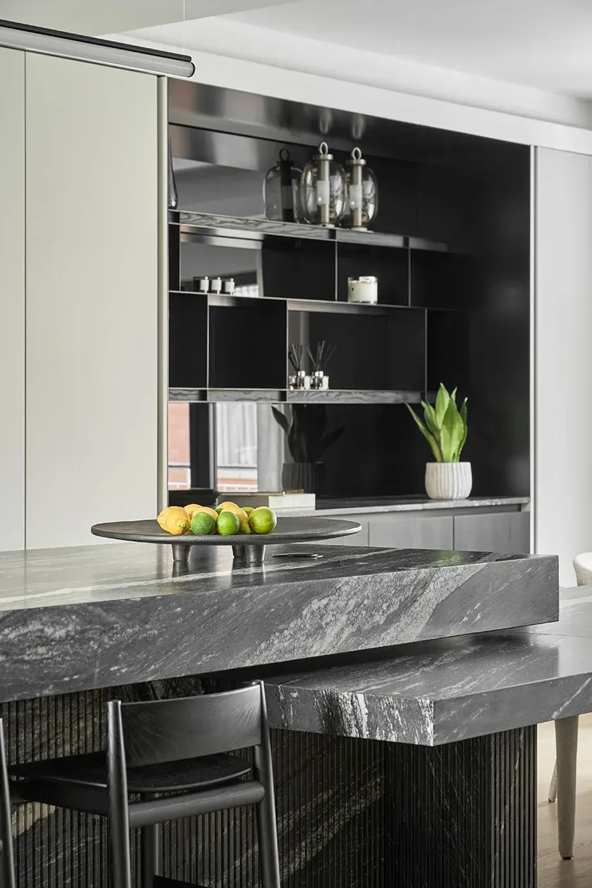 Sleek black marble kitchen island with layered countertops, dark open shelving, and decorative lemons and limes on a tray in a modern luxury home.