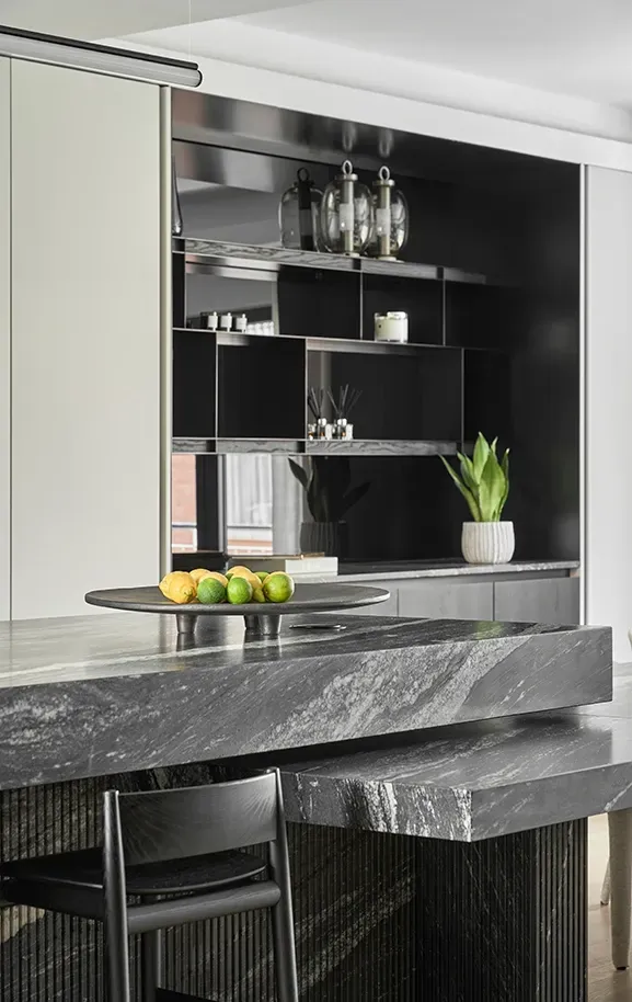 Sleek black marble kitchen island with layered countertops, dark open shelving, and decorative lemons and limes on a tray in a modern luxury home.
