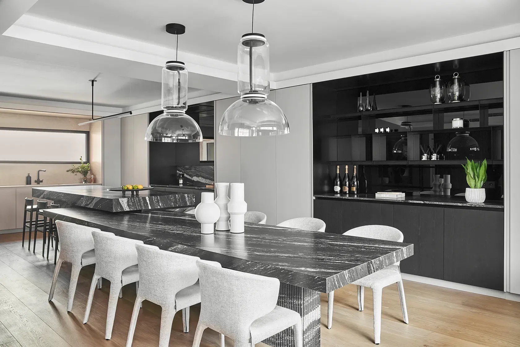 Luxury open-plan kitchen and dining area with black marble surfaces, soft grey chairs, and large glass pendant lights by LUV Studio in Madrid.