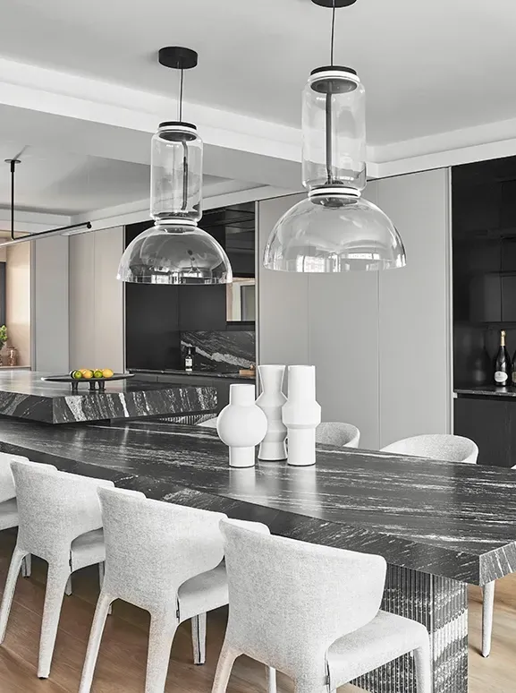 Luxury open-plan kitchen and dining area with black marble surfaces, soft grey chairs, and large glass pendant lights by LUV Studio in Madrid.