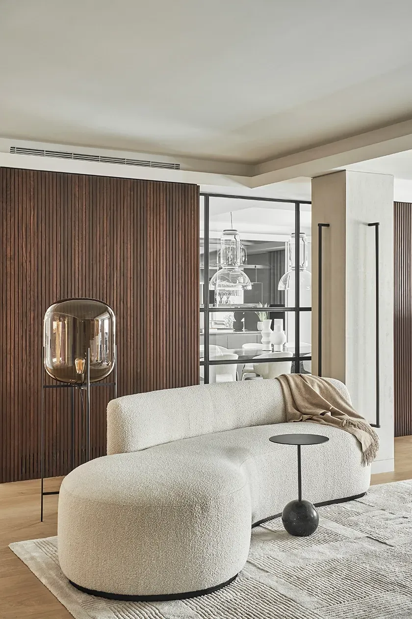 Cozy corner with textured curved sofa and smoked glass floor lamp, offering a glimpse into the elegant dining area in this refined LUV Studio design.