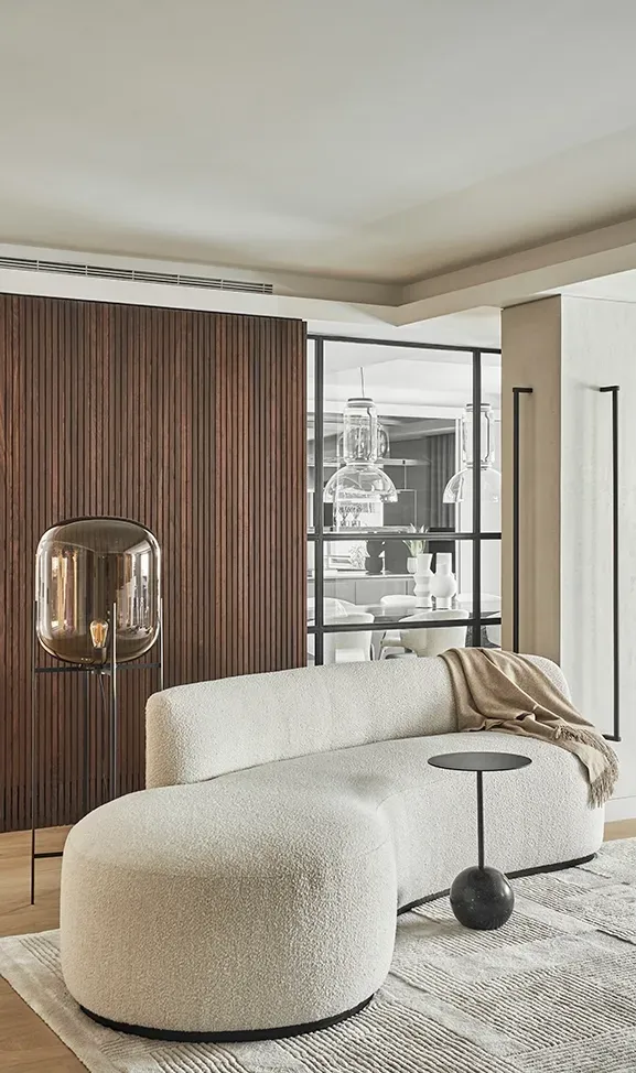 Cozy corner with textured curved sofa and smoked glass floor lamp, offering a glimpse into the elegant dining area in this refined LUV Studio design.