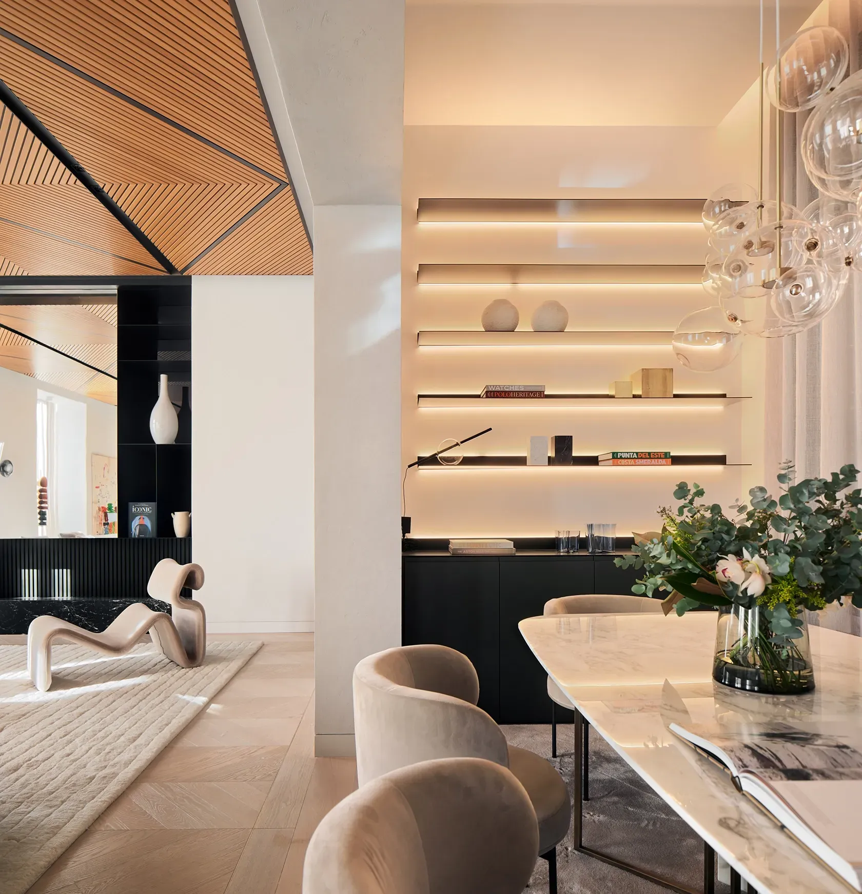 Dining room with marble table and backlit shelves, featuring luxury interior architecture.