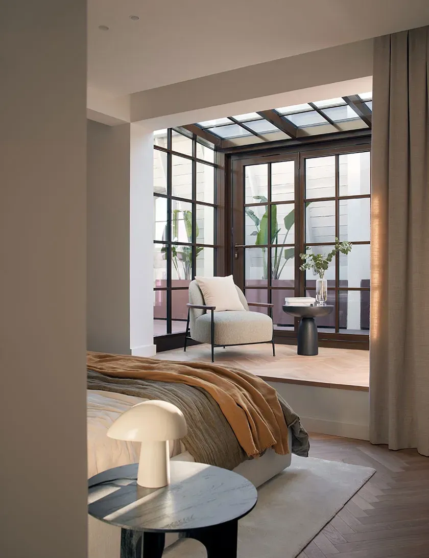 Penthouse bedroom with soft natural light, earthy textiles and access to a glass-enclosed terrace garden.