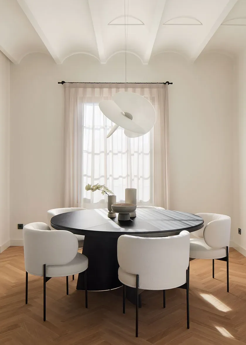 Dining area with vaulted ceiling, round black table and modern white chairs, evoking luxury and architectural purity.