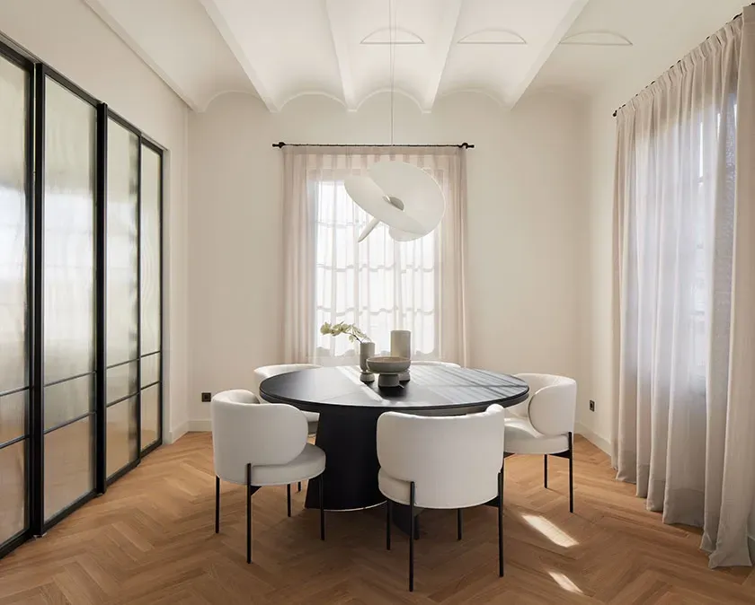 Dining area with vaulted ceiling, round black table and modern white chairs, evoking luxury and architectural purity.
