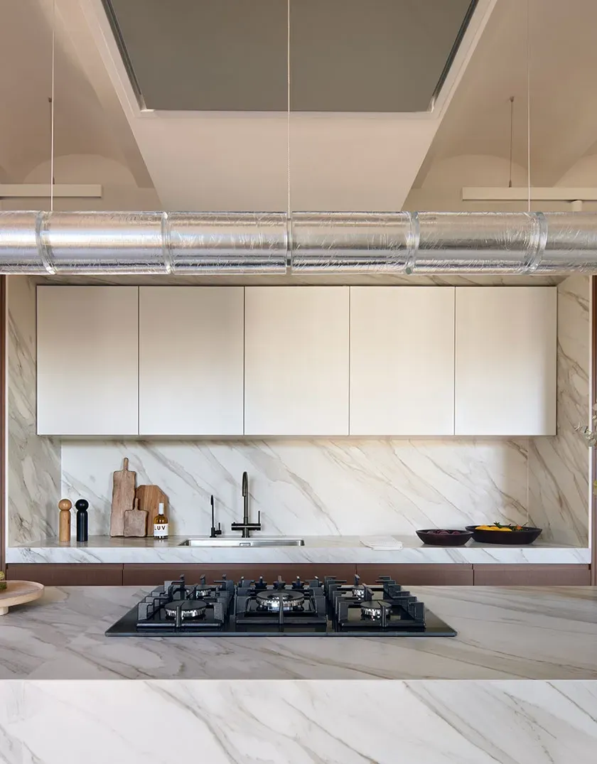 Modern kitchen with marble island, gas hob and decorative greenery in a refined luxury architectural space.