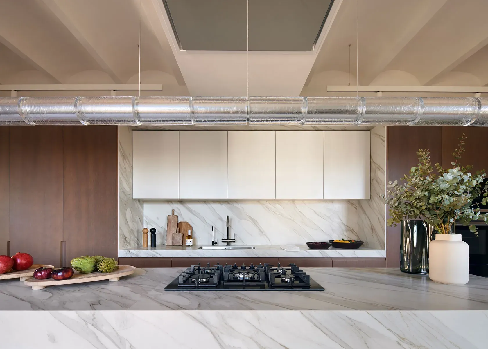 Modern kitchen with marble island, gas hob and decorative greenery in a refined luxury architectural space.