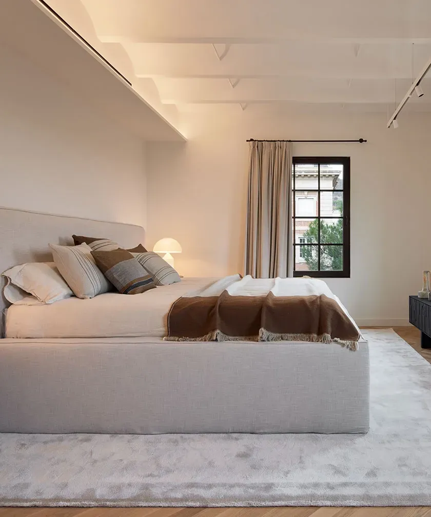 Serene master bedroom with soft lighting, upholstered bed and large windows in a luxury penthouse.