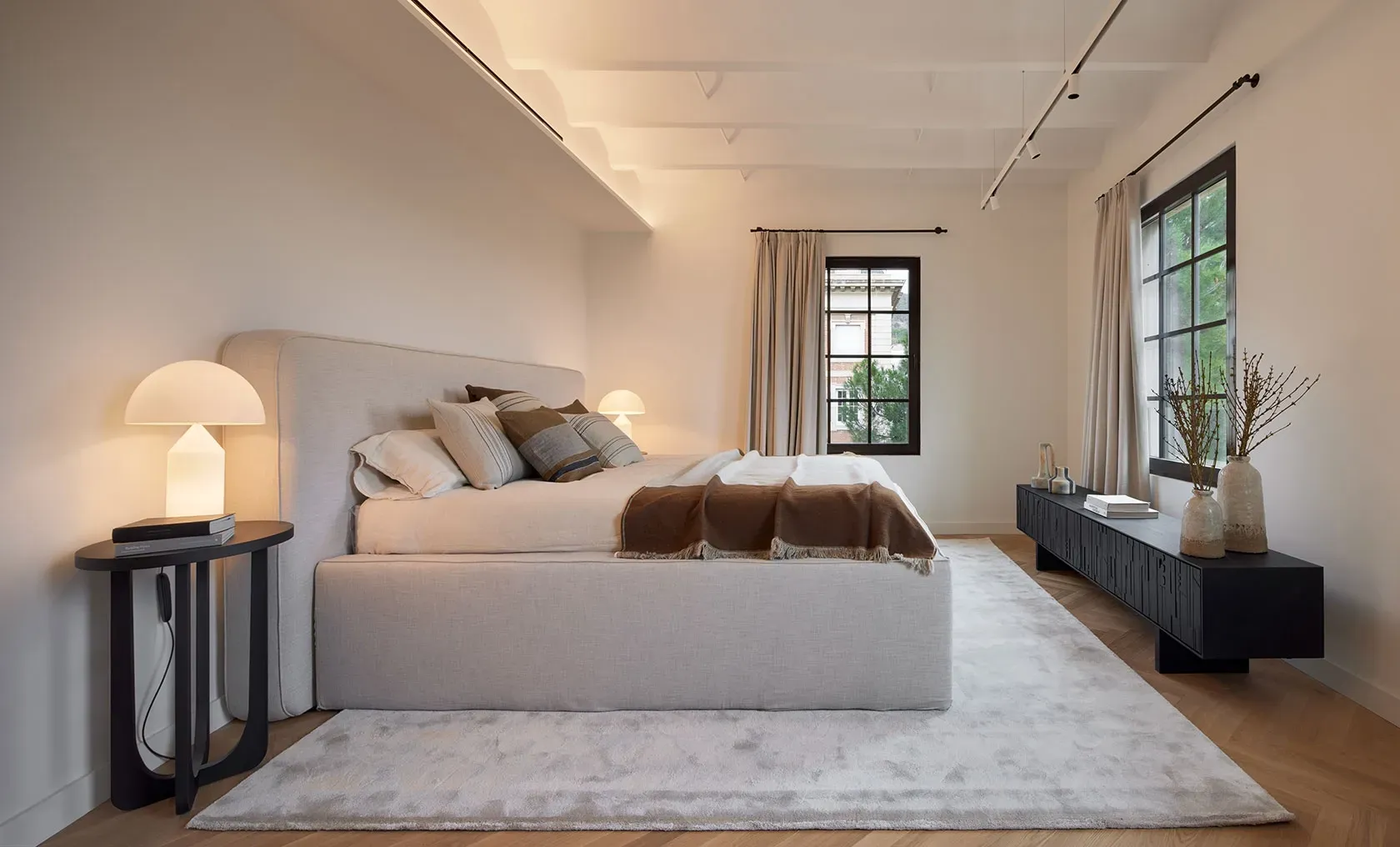 Serene master bedroom with soft lighting, upholstered bed and large windows in a luxury penthouse.