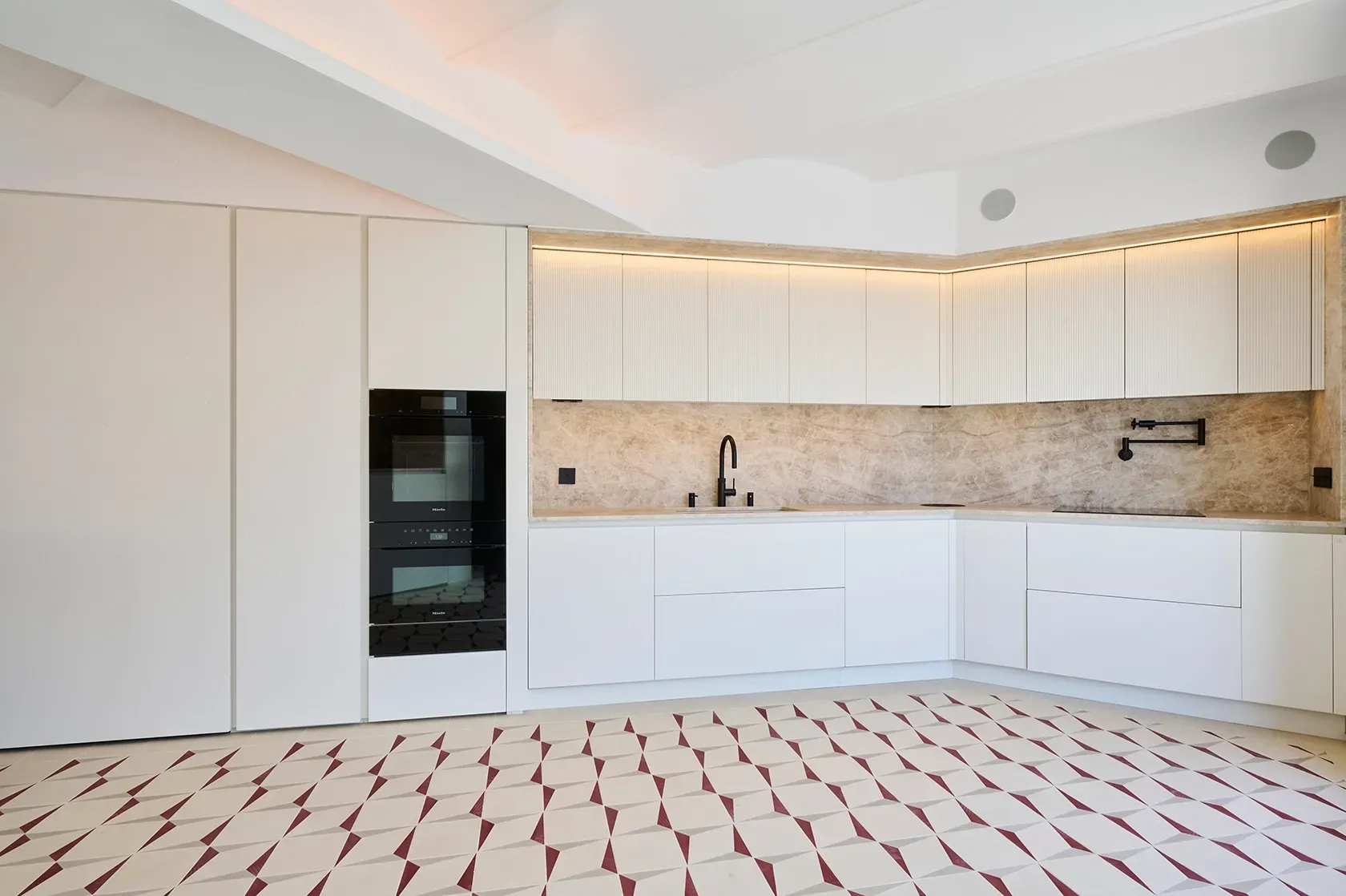 Minimalist kitchen with white cabinetry, marble backsplash, and patterned tile floor, featuring integrated appliances and warm ambient lighting.