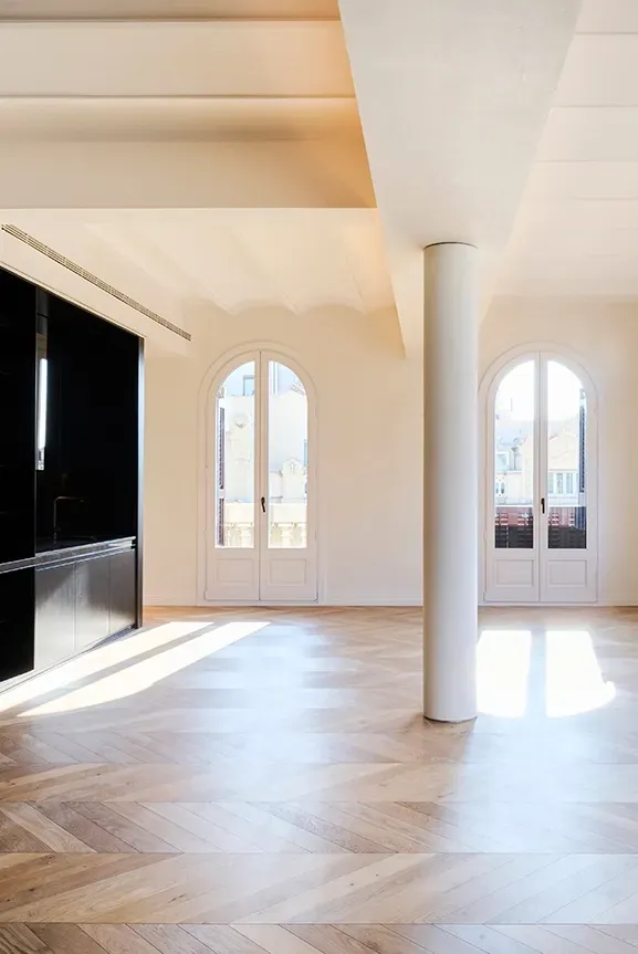 Panoramic view of a bright interior with arched windows, black shelving, and a central white column, blending historic charm and modernity.