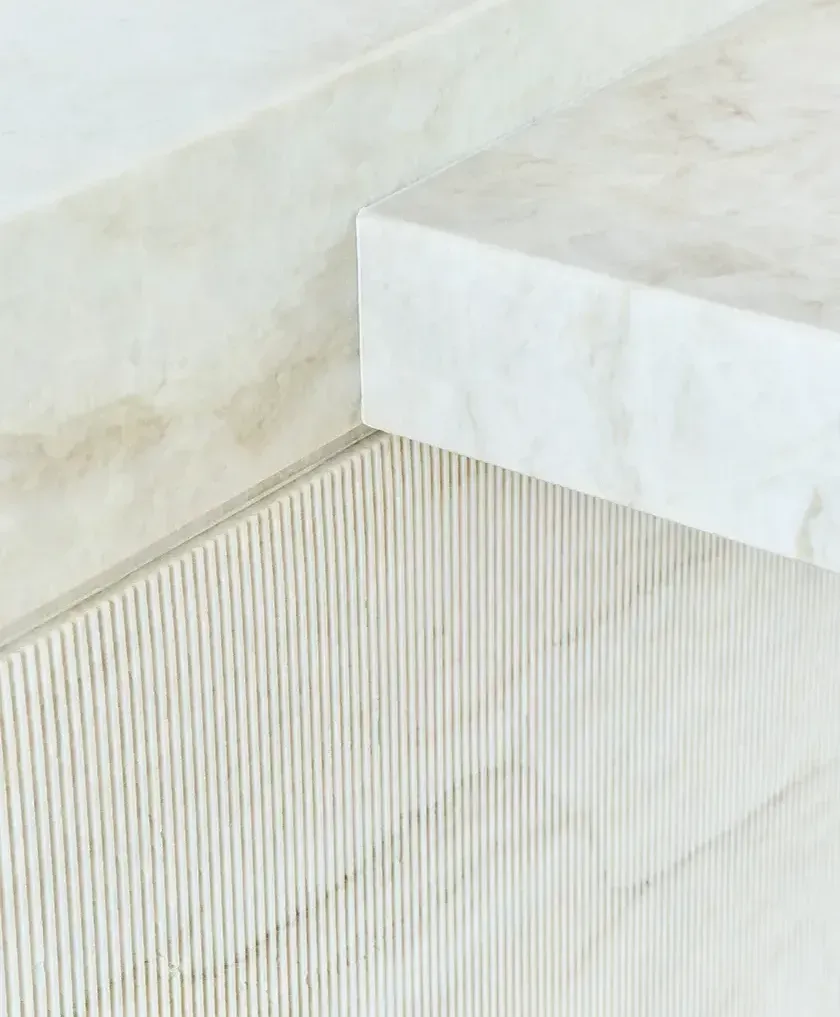 Close-up of natural stone island with fluted marble detailing in a minimalist kitchen setting.