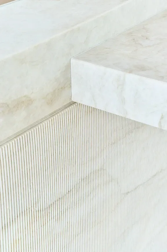 Close-up of natural stone island with fluted marble detailing in a minimalist kitchen setting.