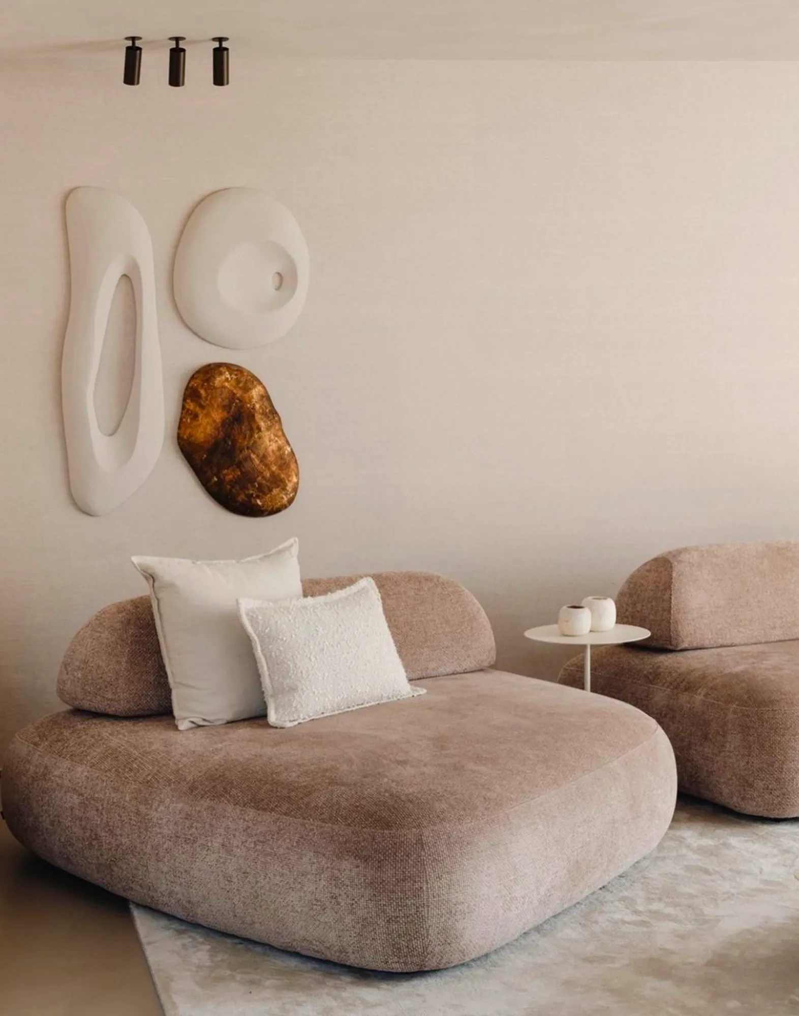 Soft beige lounge chairs with organic shapes and sculptural wall decor in a serene, minimalist living space.