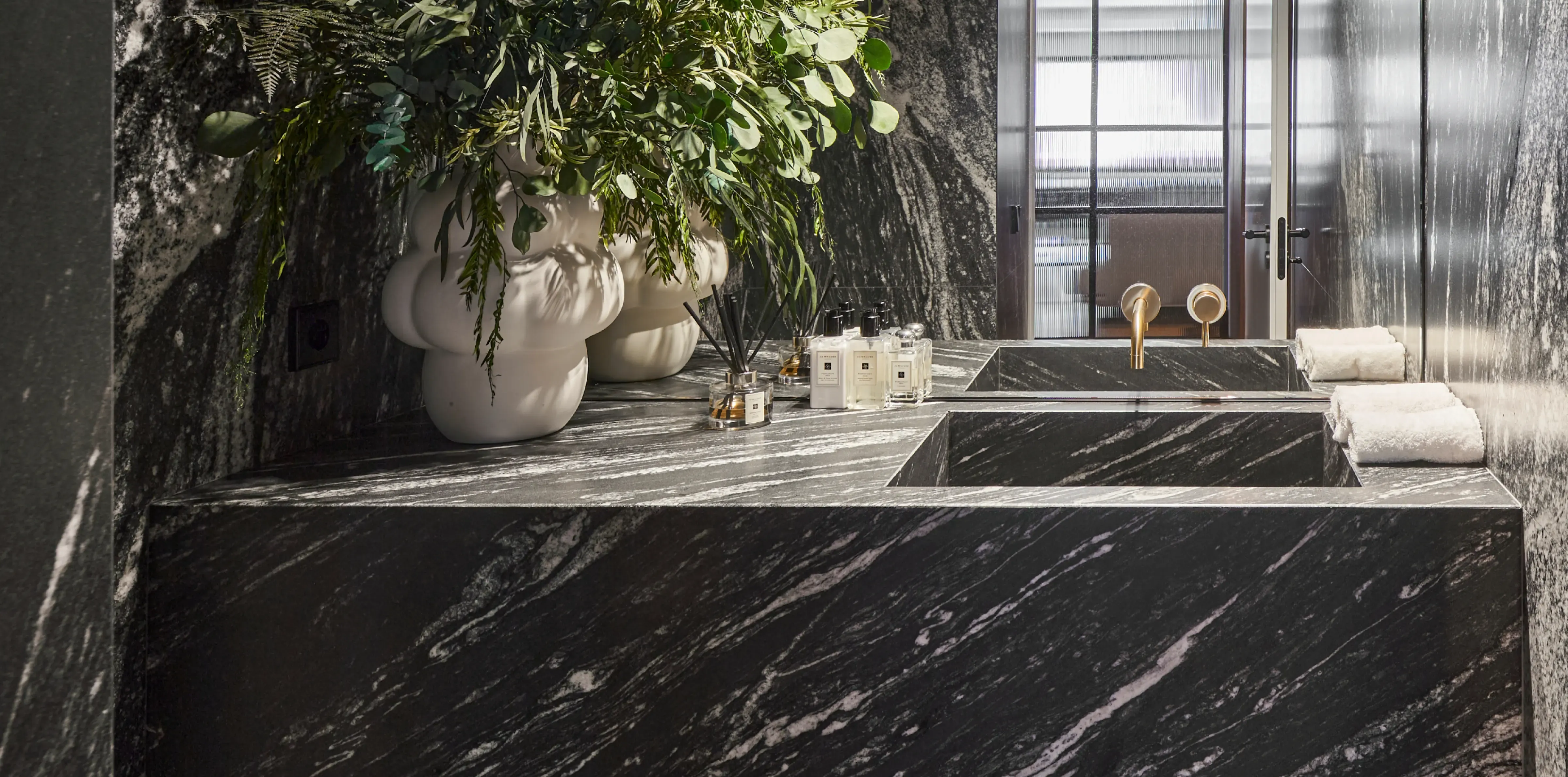 Luxury bathroom with black marble sink, gold fixtures and sculptural ceramic vase