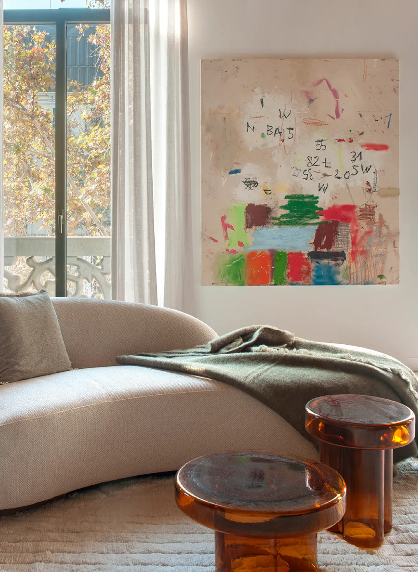 Living room with abstract artwork on white wall, curved cream sofa and amber glass tables