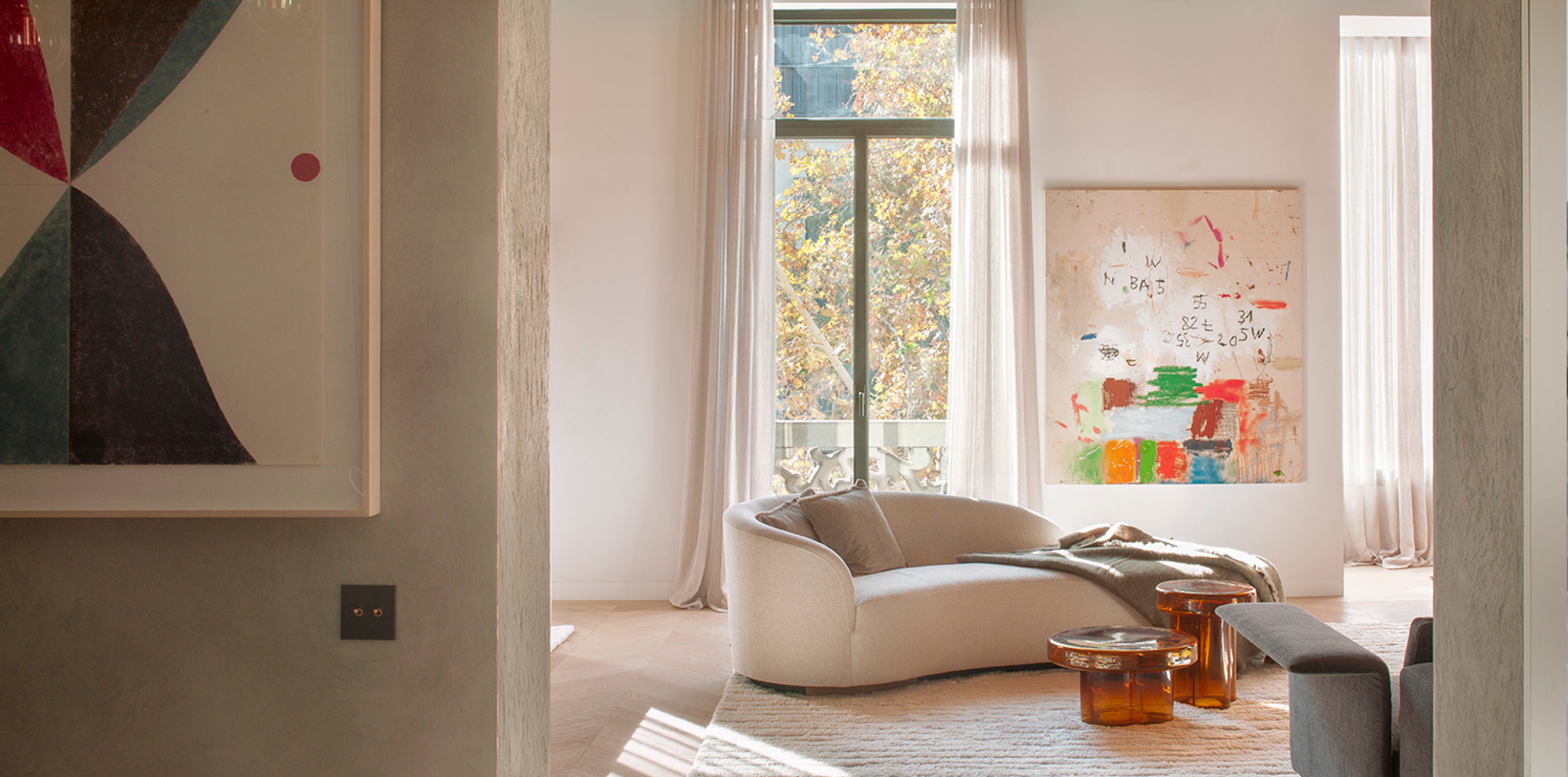 Living room with abstract artwork on white wall, curved cream sofa and amber glass tables