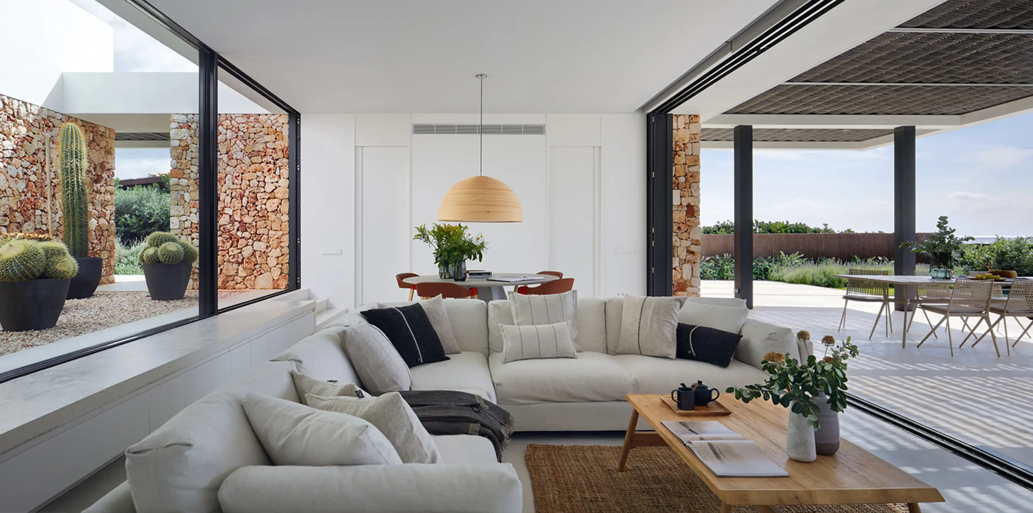 Interior living room with floor-to-ceiling windows, neutral-toned furniture, and cactus-filled patio views.