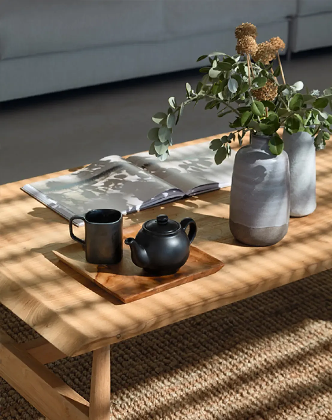 Close-up of a coffee table with ceramic vases, a teapot, and an open book in a cozy interior.