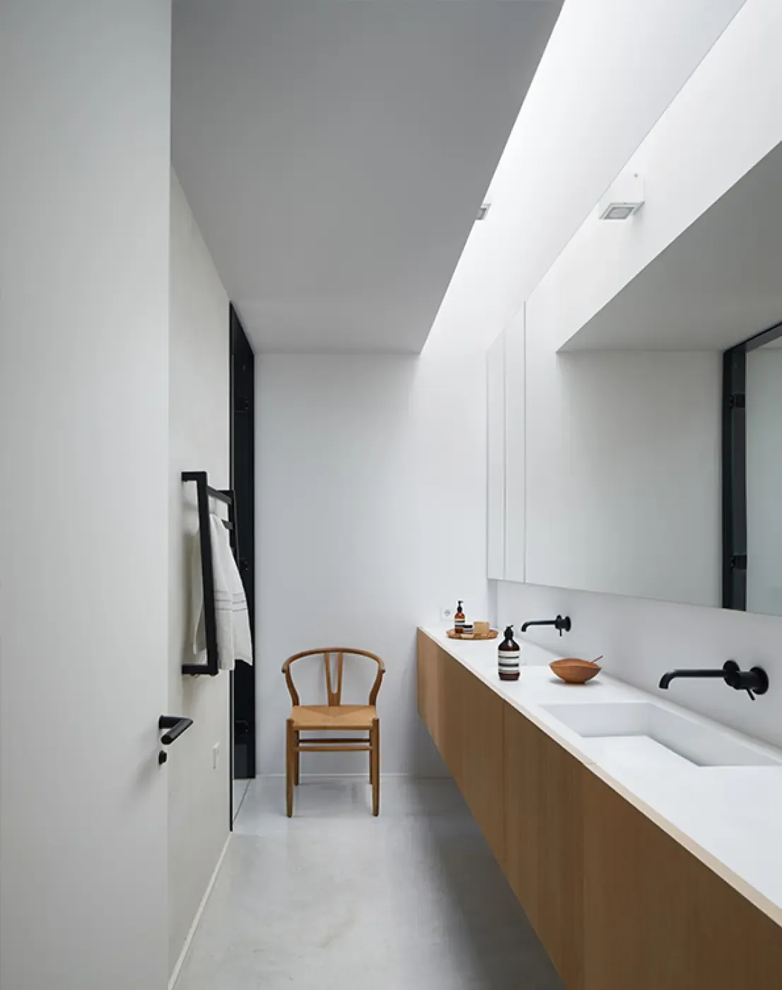Bright modern bathroom with white walls, wood vanity, and natural light filtering from a skylight.