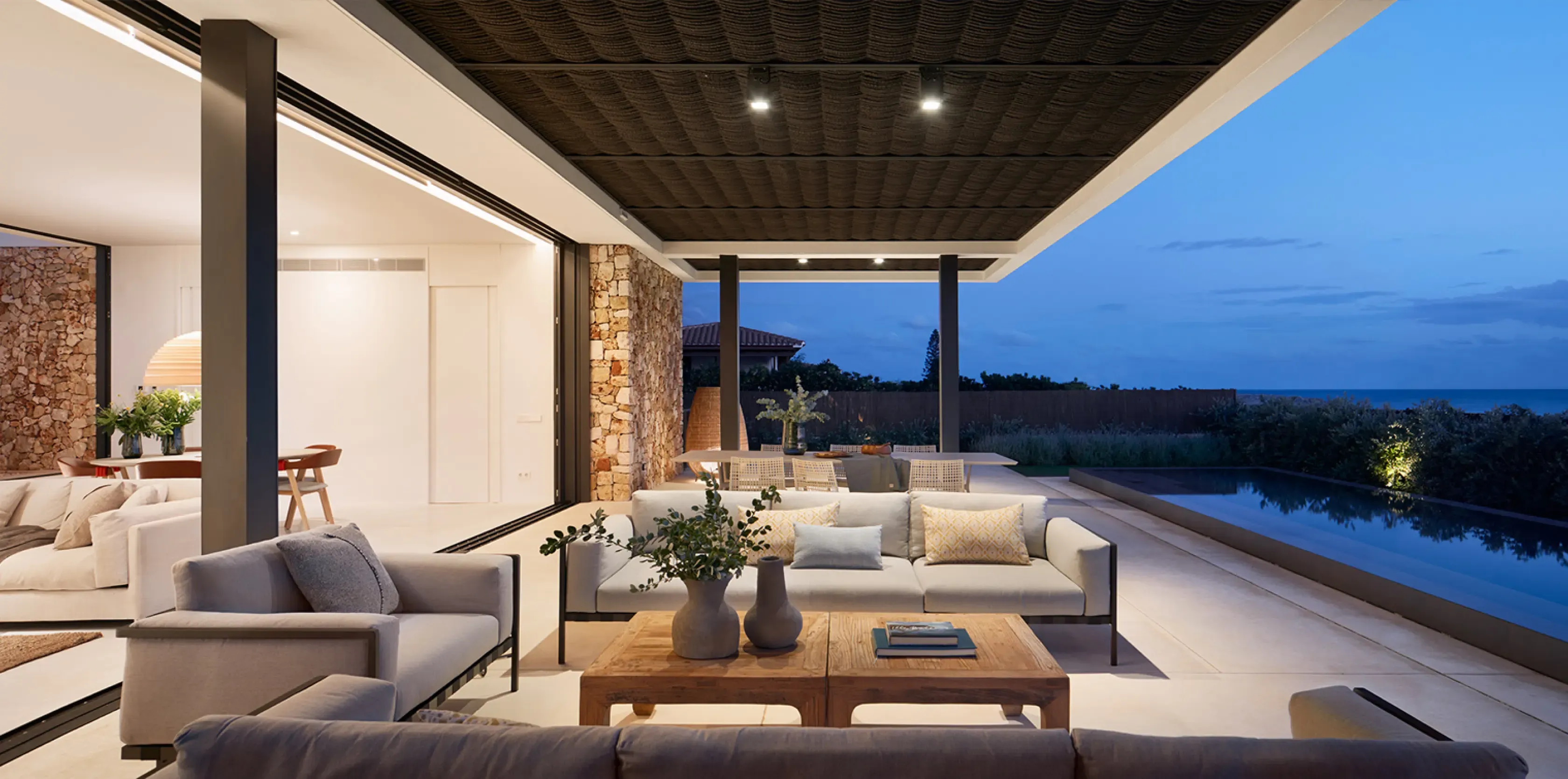 Seamless transition between indoor and outdoor living with poolside seating and ocean horizon at twilight.