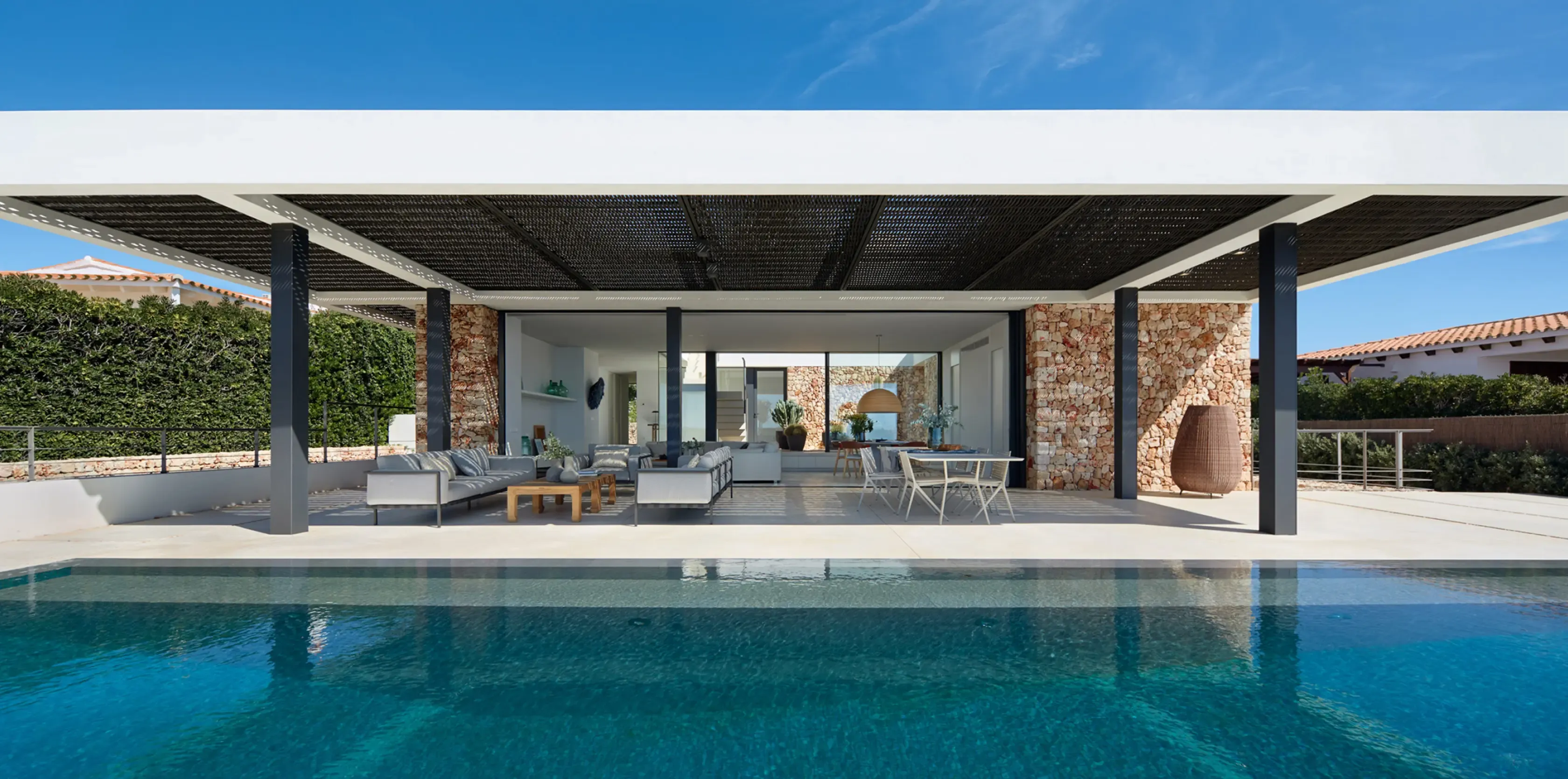 Outdoor view of the minimalist villa with pergola, stone walls, and swimming pool reflecting the modern Mediterranean design.