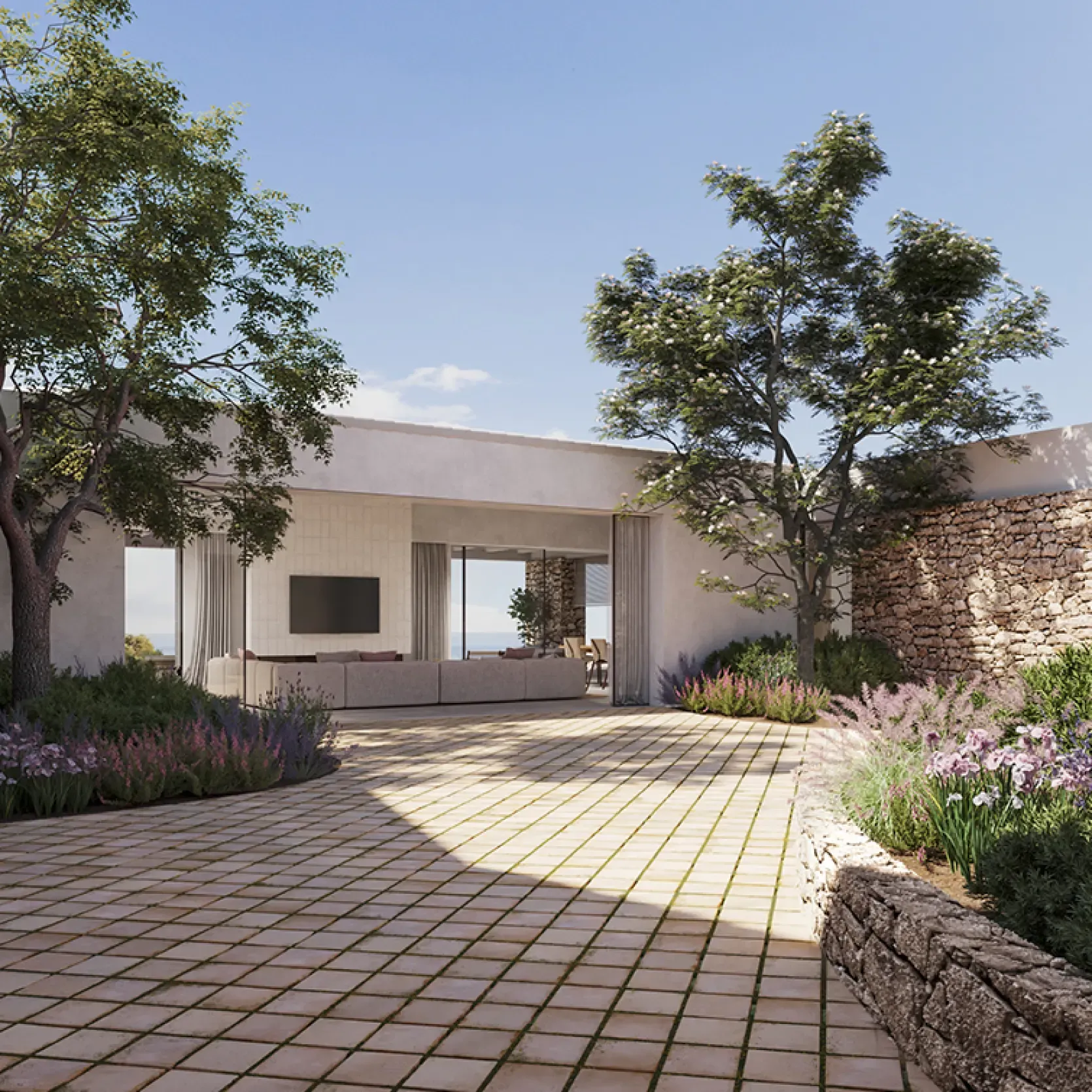 Stone-paved courtyard with lush Mediterranean landscaping and a modern open-plan villa by LUV Studio in Menorca.