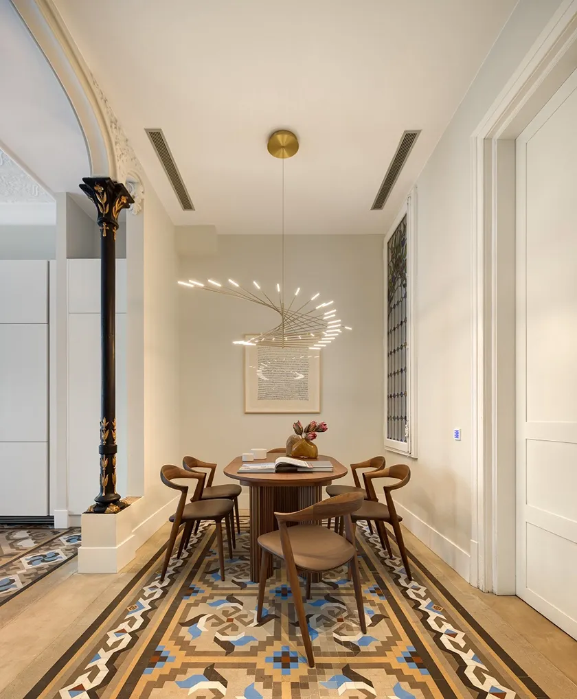 Comedor de Casa Oller con mesa de madera, sillas de diseño tapizadas en cuero, lámpara escultórica y suelo hidráulico.