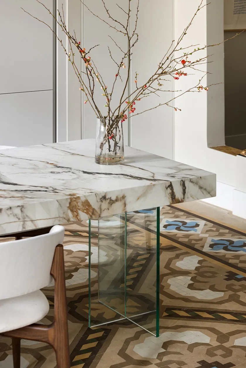 Detalle de la isla de cocina de Casa Oller, con superficie veteada, soporte de vidrio transparente y pavimento hidráulico.