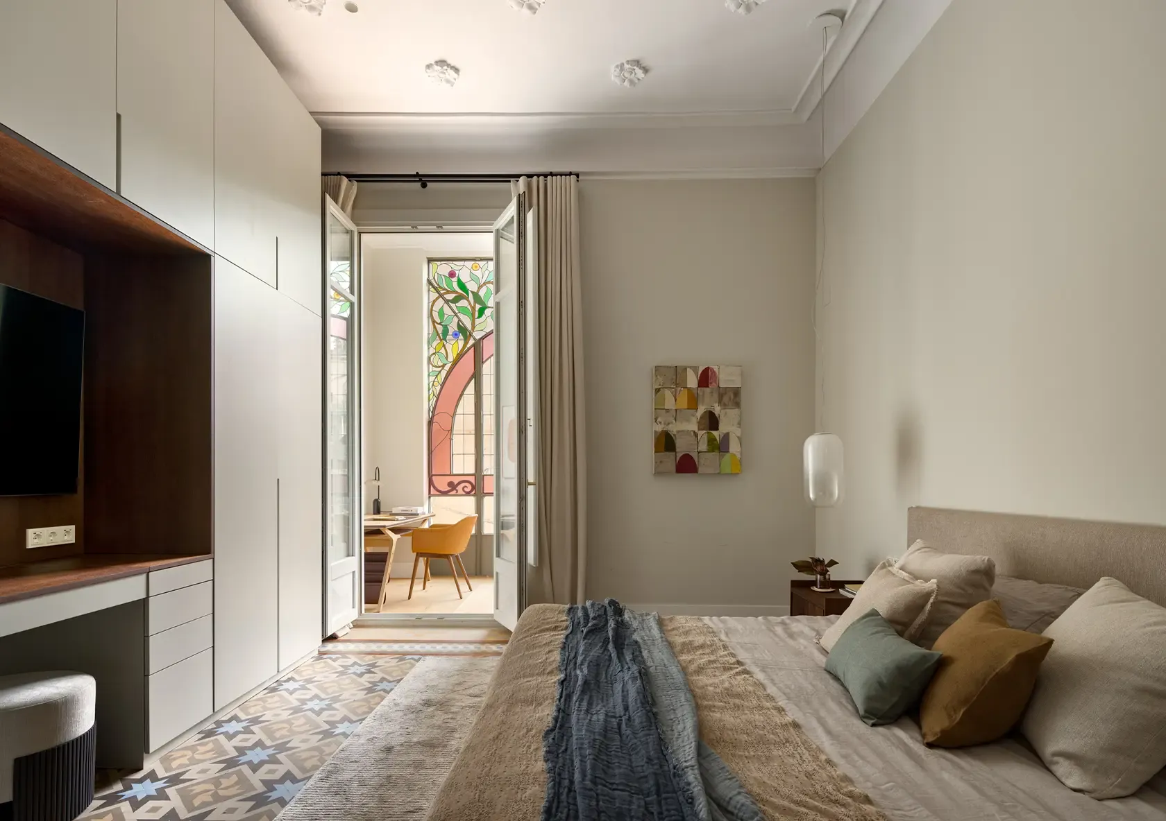Dormitorio de Casa Oller con cabecero tapizado, textiles naturales en tonos neutros y suelos hidráulicos modernistas.