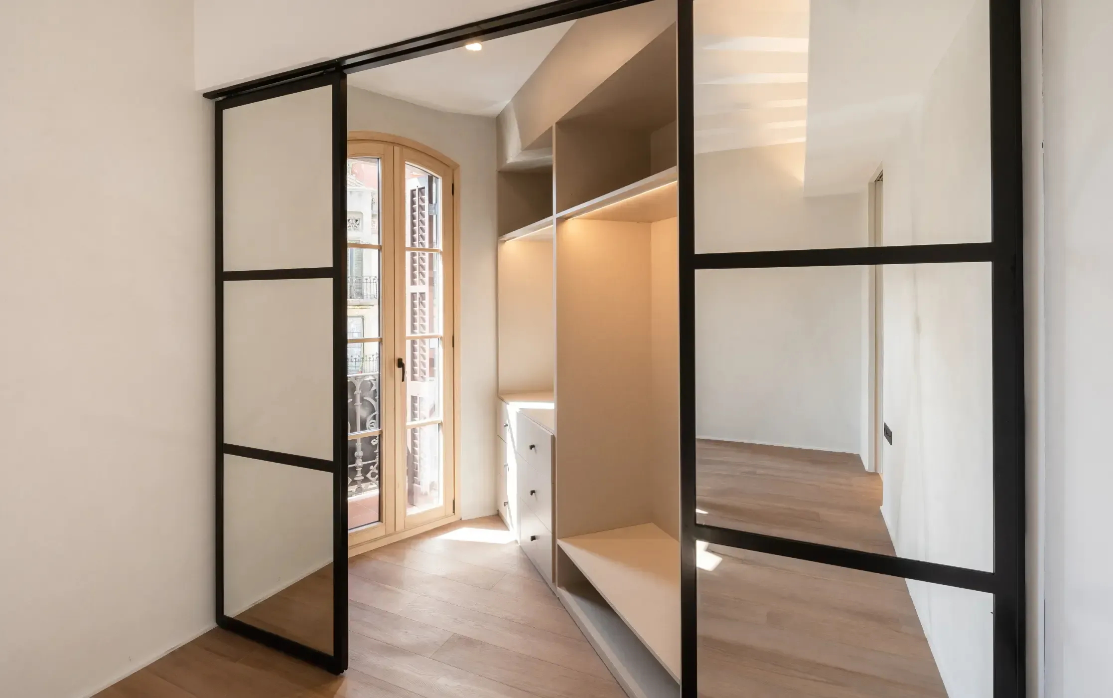 Minimalist walk-in closet with natural light and sliding glass doors, designed by Luv Studio in Barcelona.