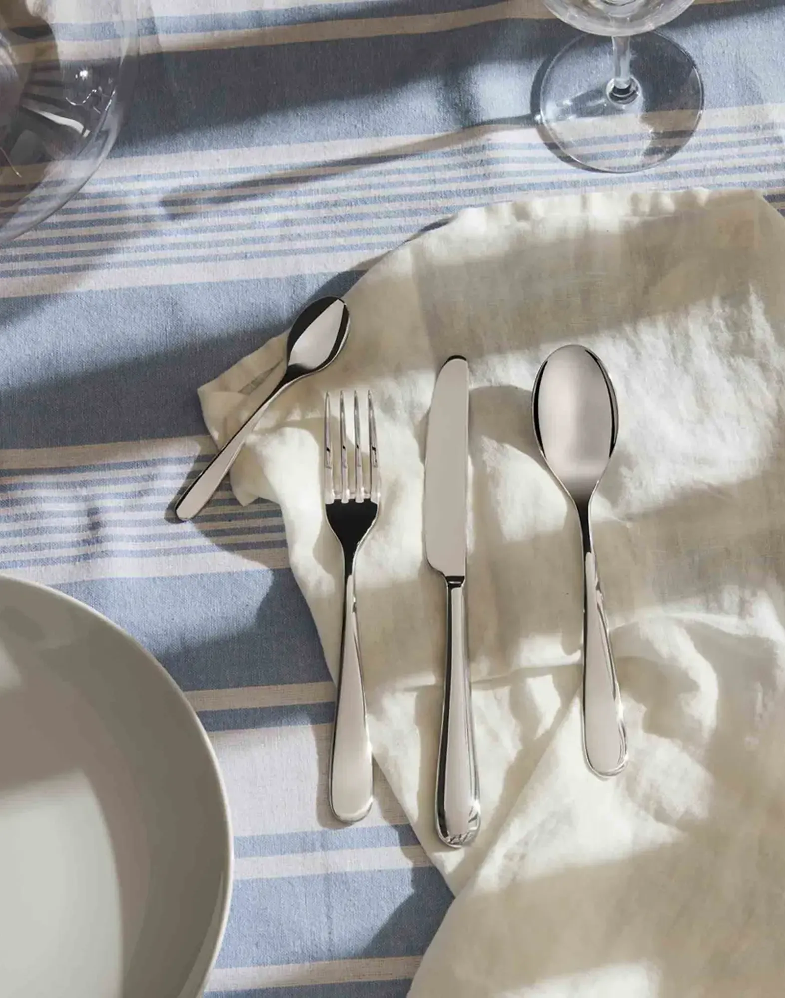 Classic polished steel flatware set on striped linen tablecloth.