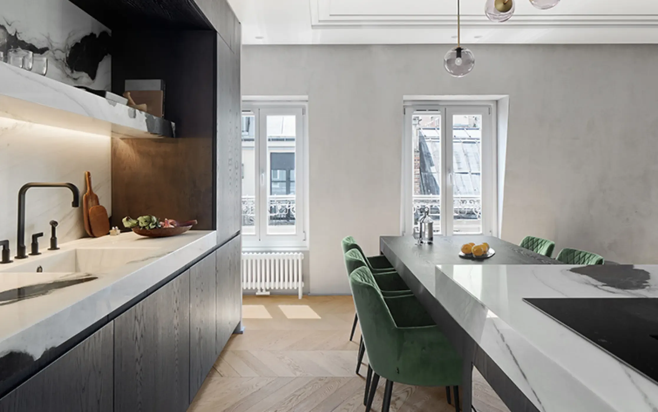 Contemporary kitchen design with long marble island, green velvet chairs, and windows framing Parisian rooftops for added charm.