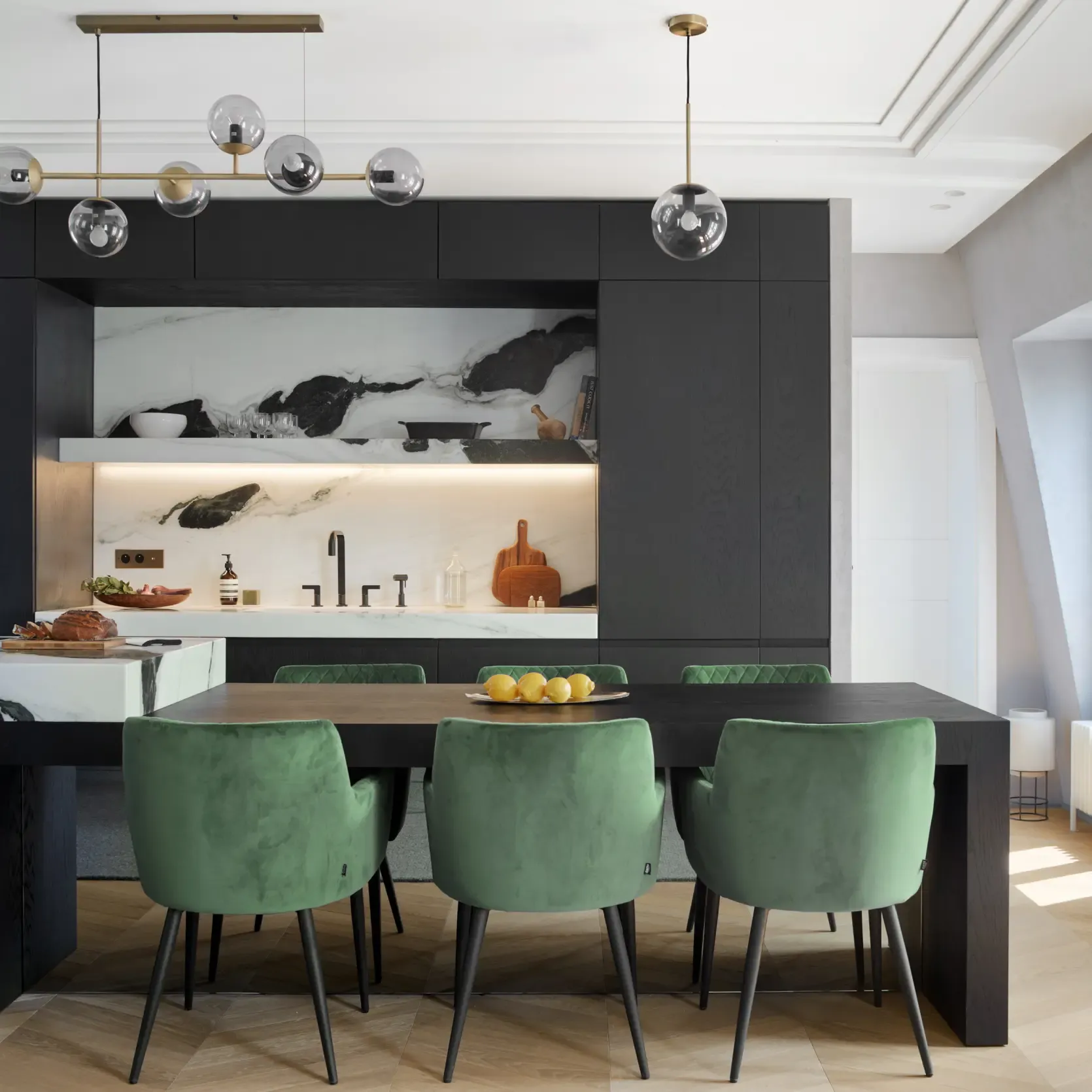 Dining and kitchen space with black cabinetry, marble surfaces, and green velvet chairs creating a refined contrast with natural wood floor.