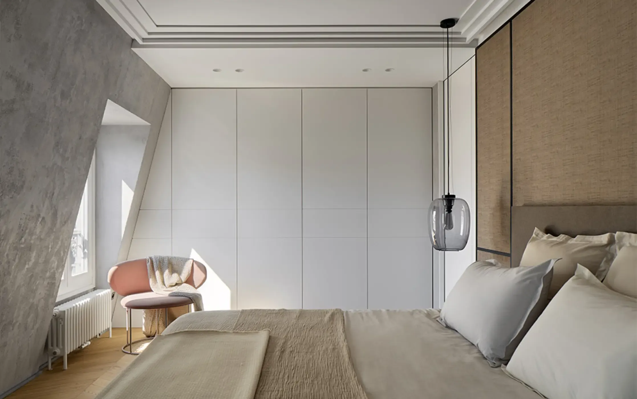 Minimalist bedroom with neutral tones, upholstered headboard, built-in white wardrobes, and soft natural light through a side window.