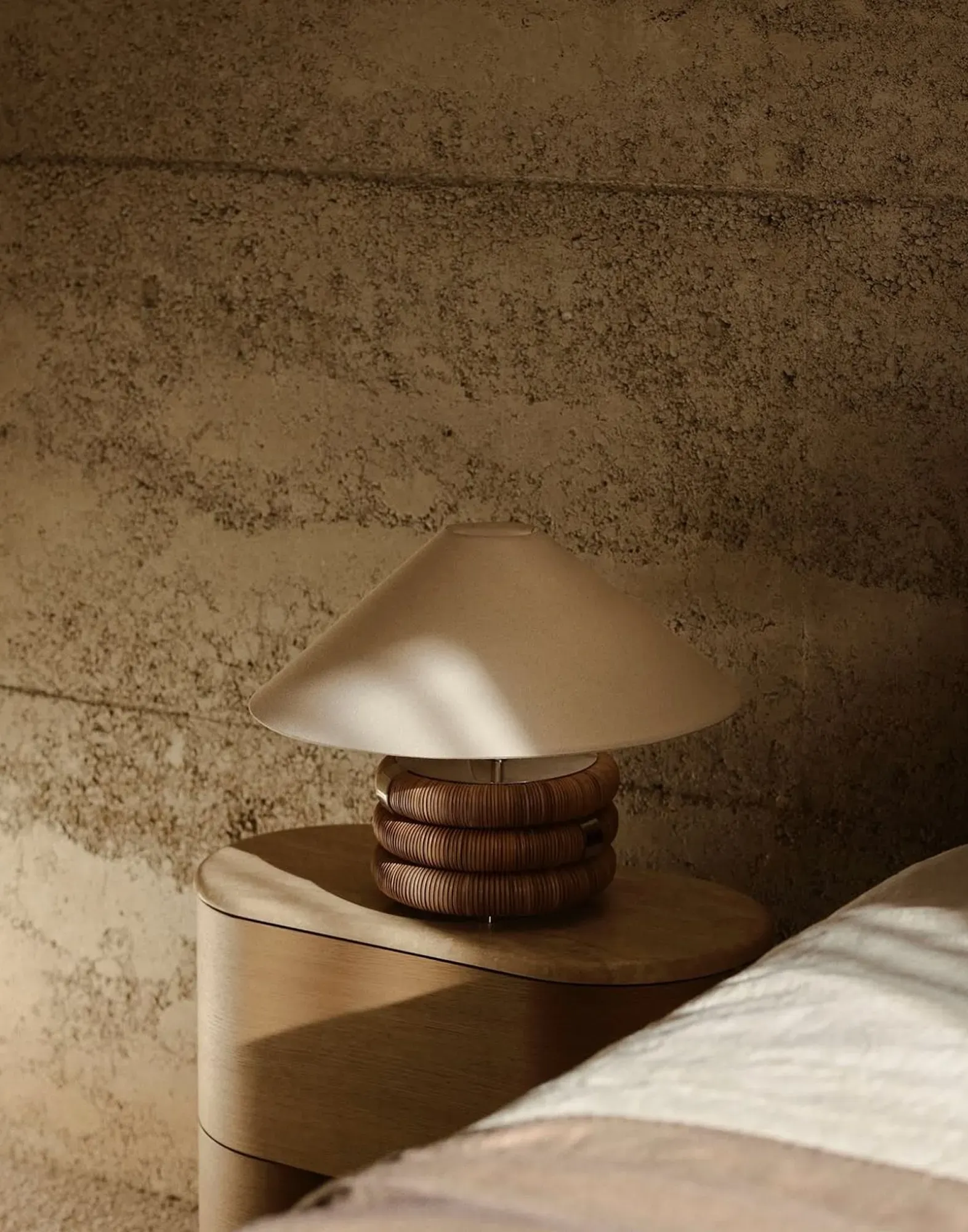 Sculptural bedside lamp with coiled rattan base and wide fabric shade in a warm-toned bedroom.