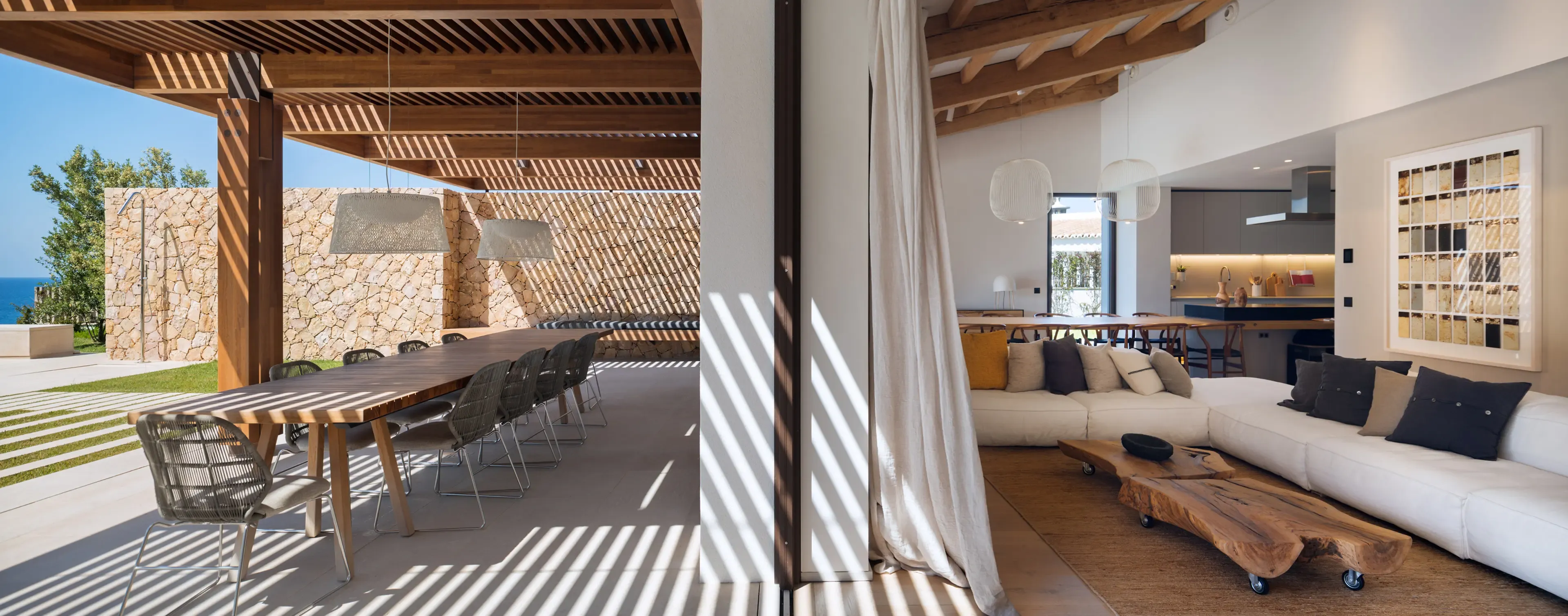 Covered terrace with long wooden dining table, wicker chairs, and stone walls, blending indoor and outdoor living by the sea.