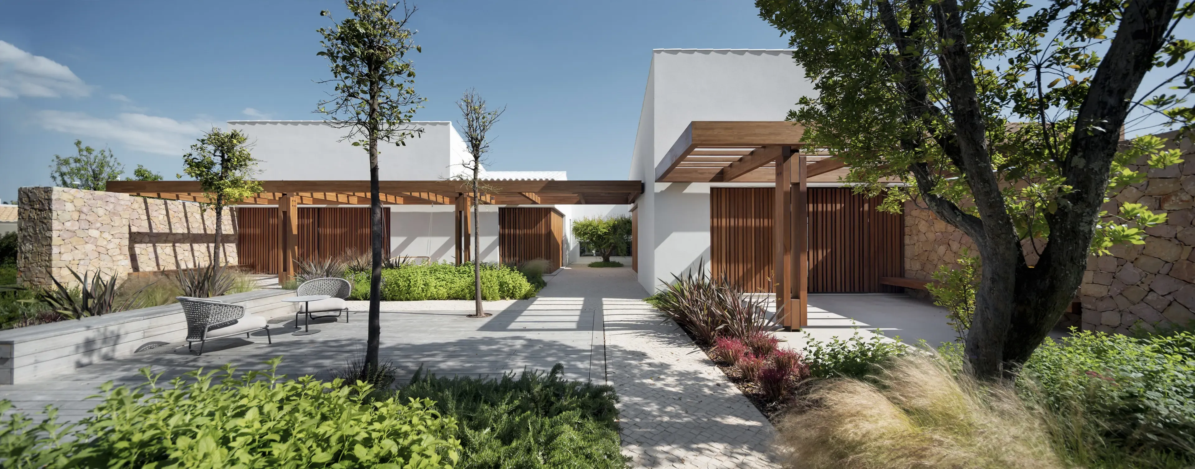 Contemporary villa façade with stone walls, wooden pergolas, and landscaped garden pathways surrounded by greenery.