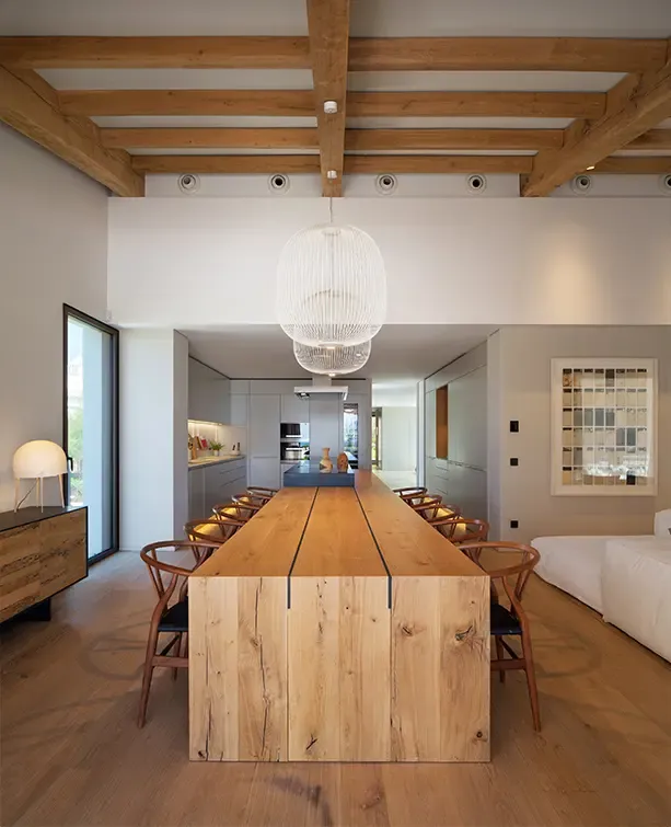 Modern dining area with long wooden table, designer chairs, exposed ceiling beams, and pendant lighting.