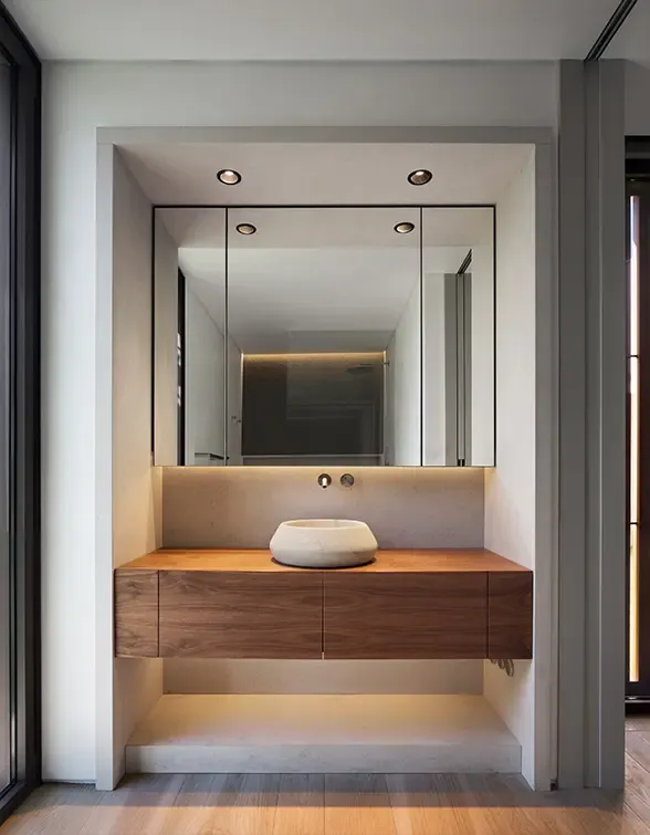 Minimalist bathroom with floating wooden vanity, stone countertop, and large mirror with integrated lighting.