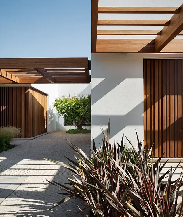 Modern courtyard view with wooden pergola, vertical slatted doors, stone paving, and lush plants enhancing the elegant luxury architectural design.