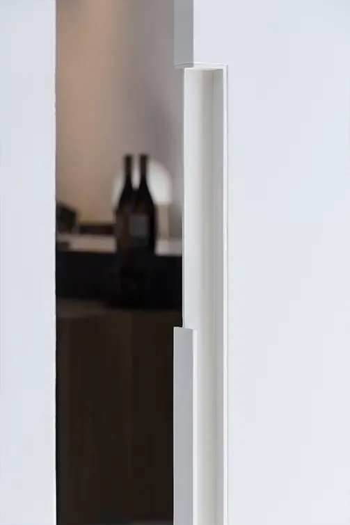 Close-up of sleek white wall with integrated handle and blurred background, highlighting minimalist architectural detail.