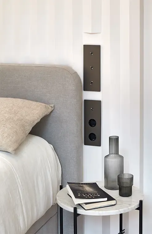 Cozy bedroom corner with upholstered headboard, marble side table, glassware, and neutral tones reflecting refined modern interior style.