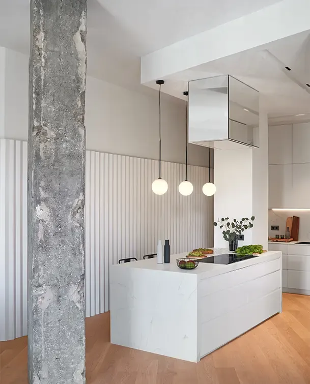 Contemporary kitchen view with marble island, pendant lights, wooden floors, and industrial column blending elegance with modern design.