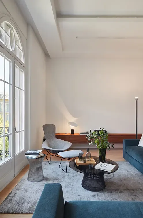 Bright living room with large window, modern armchair, coffee table, and blue sofa enhancing the sophisticated luxury apartment interior.