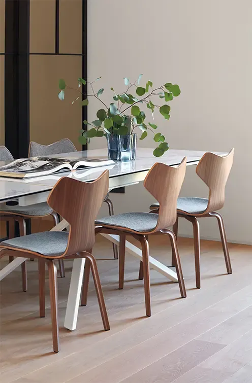 Modern dining area with wooden chairs, marble-top table, and decorative greenery, creating a refined contemporary interior atmosphere.