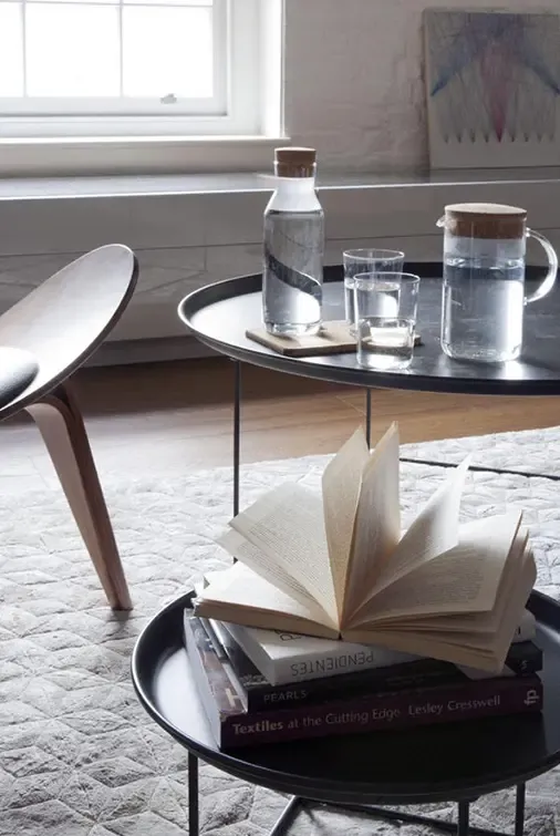 Close-up of coffee table with glass carafe, water glasses, and open book, creating a cozy modern detail in a luxury apartment living room.
