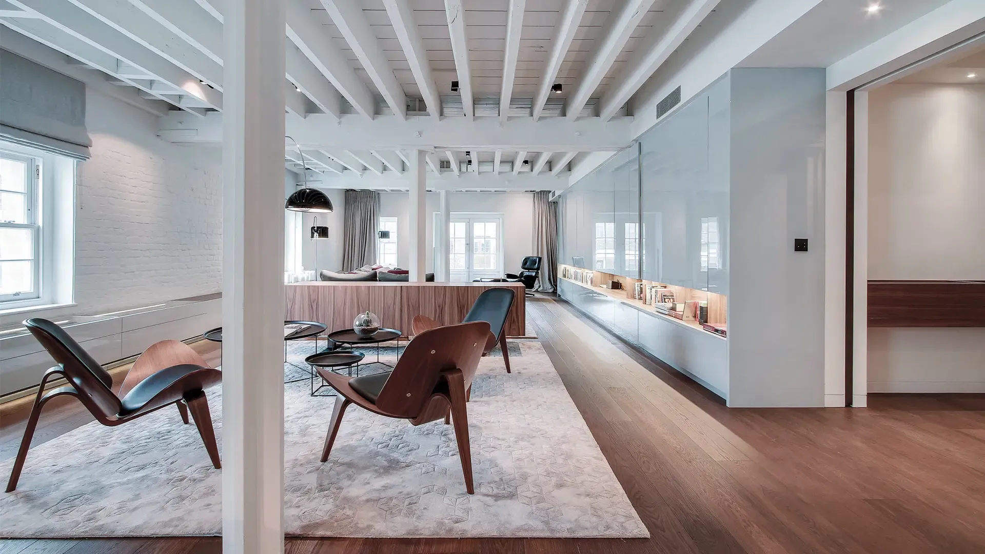Open-plan living space with exposed beams, wooden flooring, designer chairs, and modern shelving, showcasing sophisticated luxury apartment design.